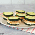 Keto Cucumber sandwiches with cream cheese and turkey on white plate, white and pink striped towel underneath plate and grey cement background