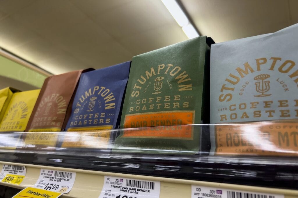 Coffee bags from Stumptown Coffee Roasters displayed on a grocery store shelf, showing different blends including "Hair Bender" in colorful packaging with yellow price tags below indicating prices around $16.99.