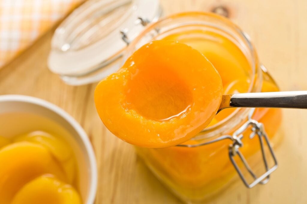 A glass jar full of peaches in syrup.