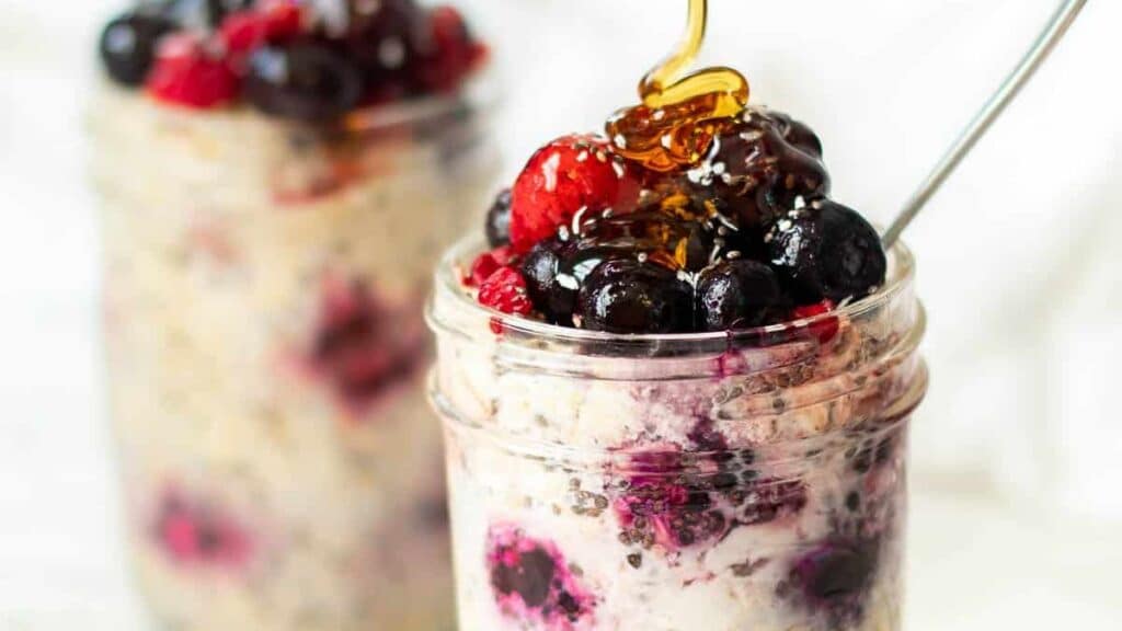 Overnight oats with frozen blueberries and strawberries with a honey drizzle on a white background.