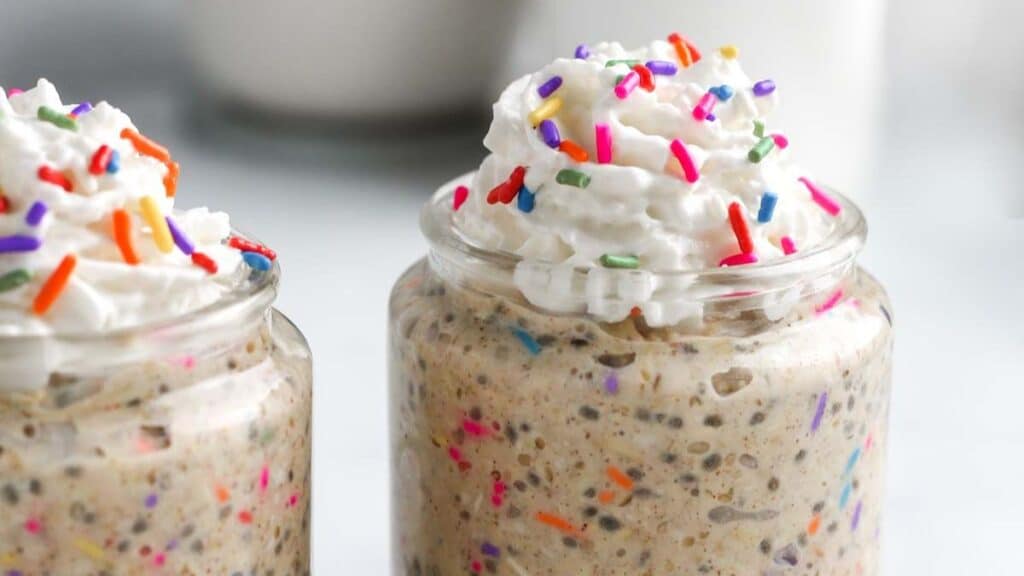 Birthday Cake Overnight Oats topped with whipped cream and sprinkles on a light background.