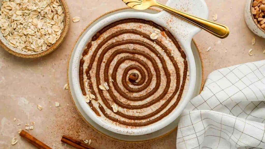 Cinnamon Roll Overnight Oats in a white bowl with a cinnamon swirl on a light background. 