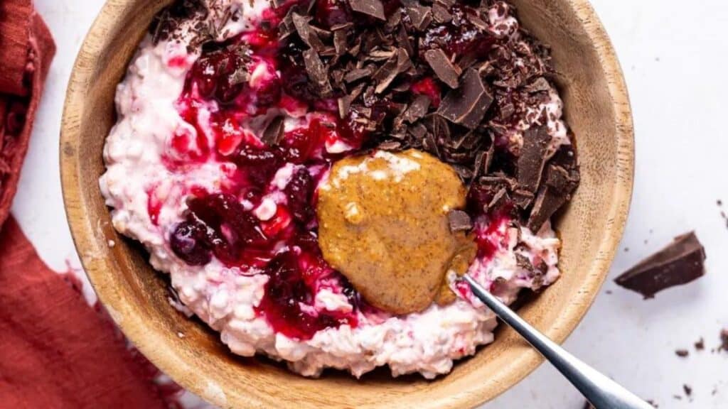 Cranberry overnight oats in a bowl with shaved chocolate and peanut butter on a light background.