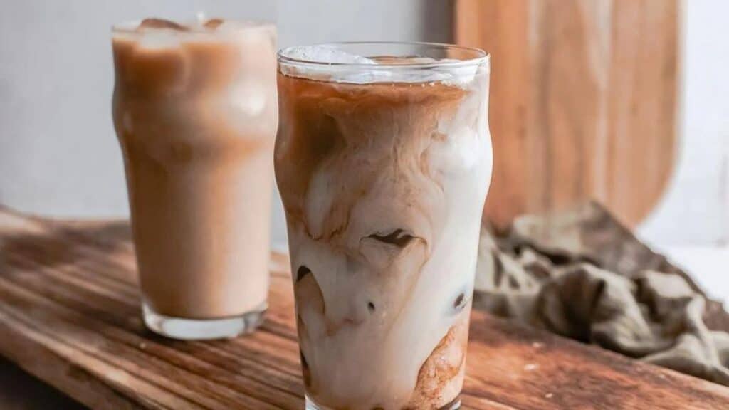 Two swirling glasses of iced espresso on a wooden counter