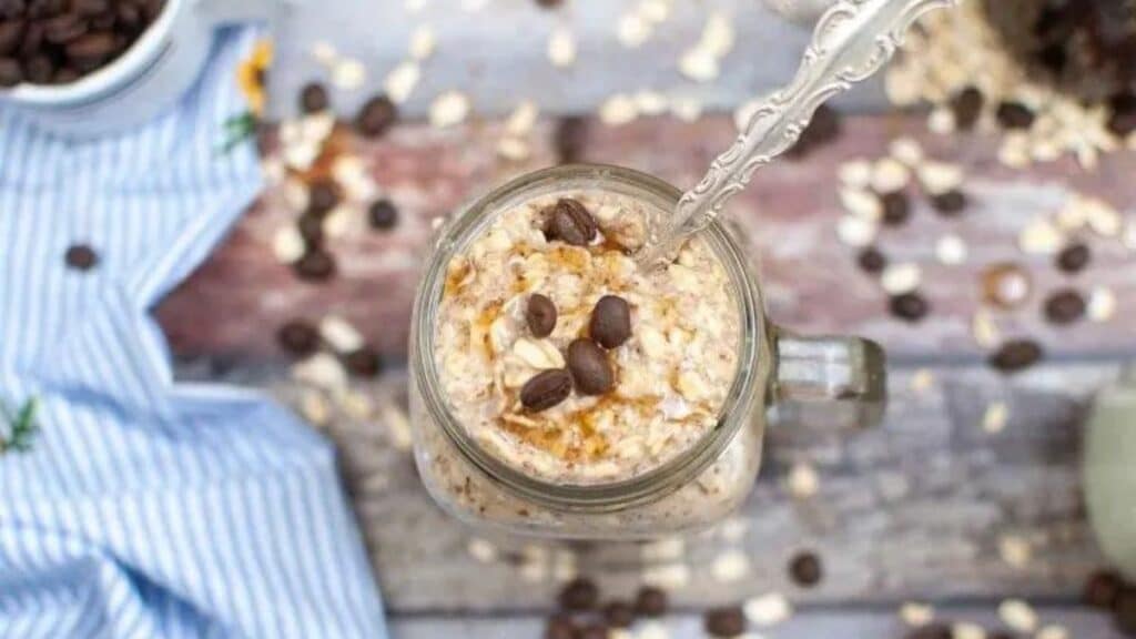 Cold Brew Overnight Oats in a mason jar with a spoon and a blue cloth in the background.
