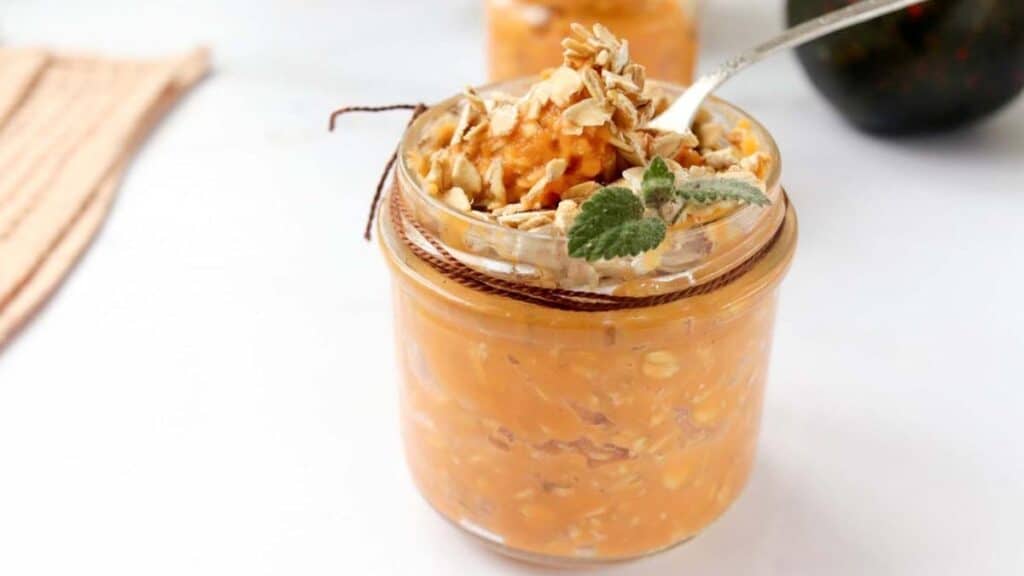 Pumpkin overnight oats in a jar with a spoon on a white background.