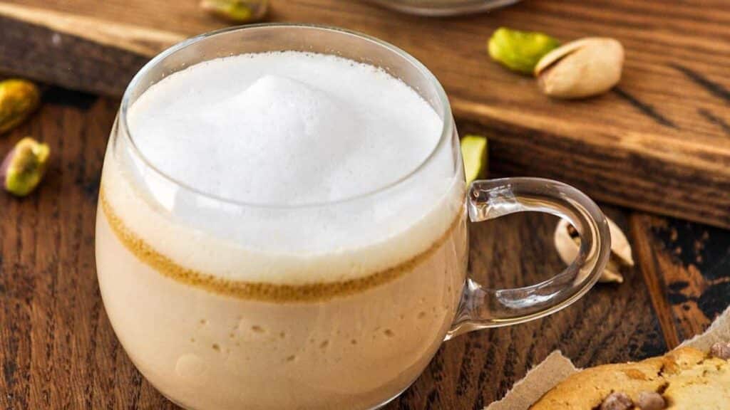 A glass of Pistachio Latte on a wooden table.