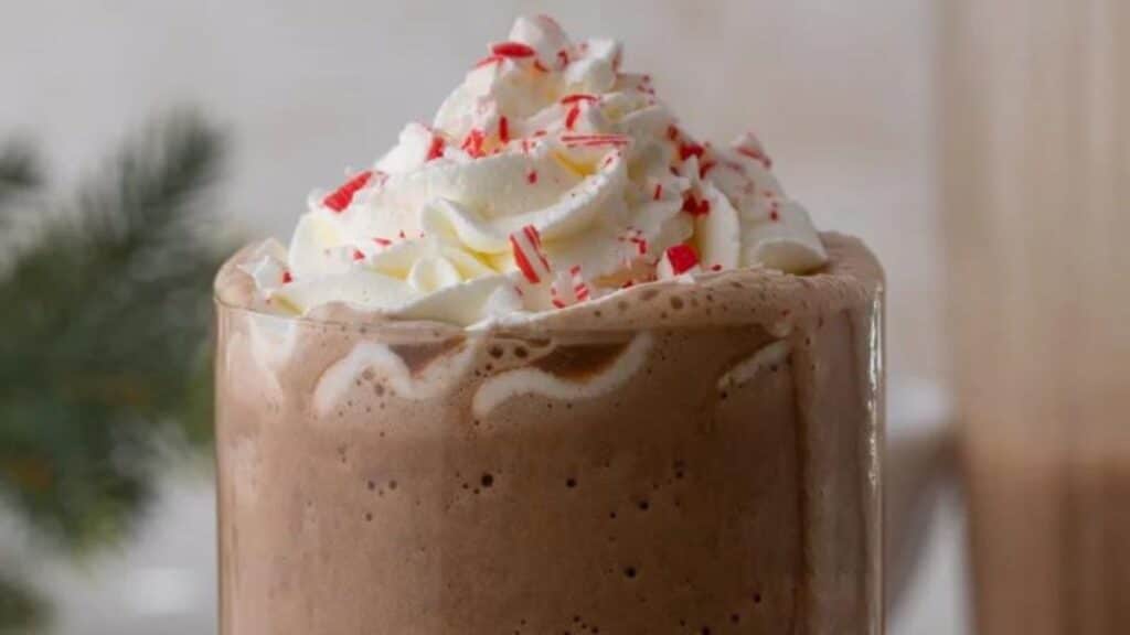A glass of Peppermint Mocha Frappuccino with whipped cream and pieces of candy cane on it.