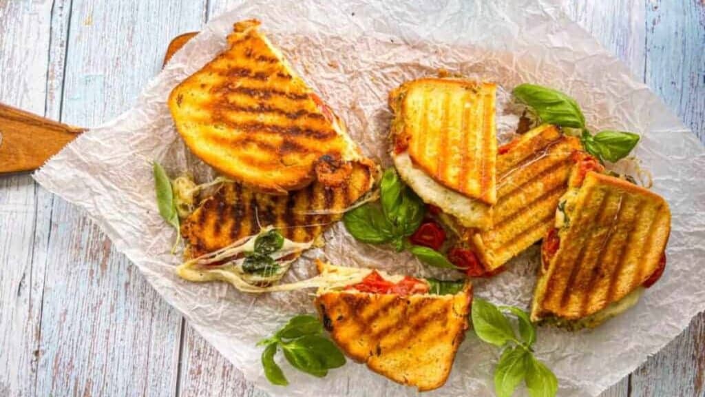 Roasted Tomato Mozzarella Panini sandwiches on a wooden cutting board on a table.