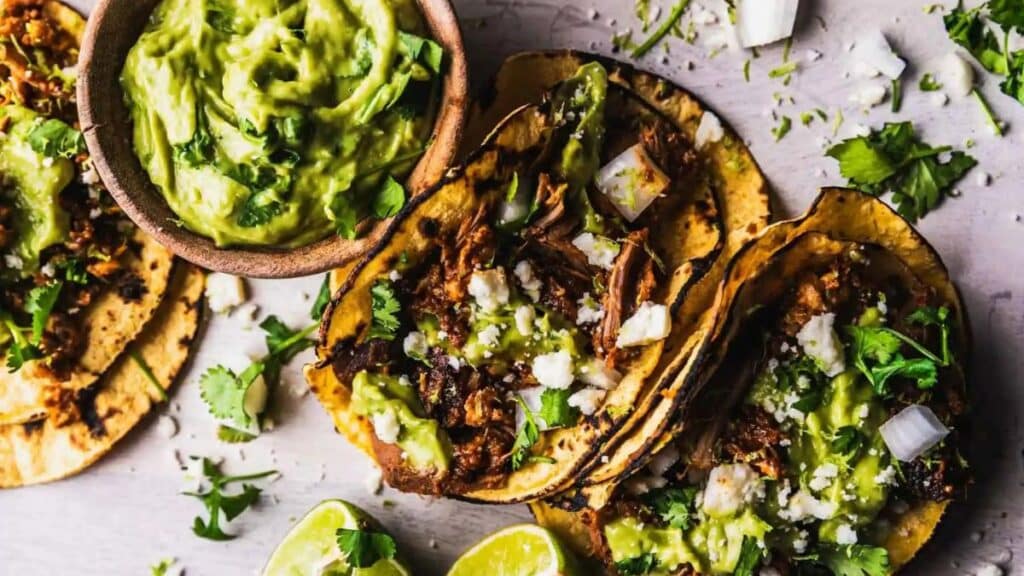 Al Pastor tacos with guacamole on a grey background.