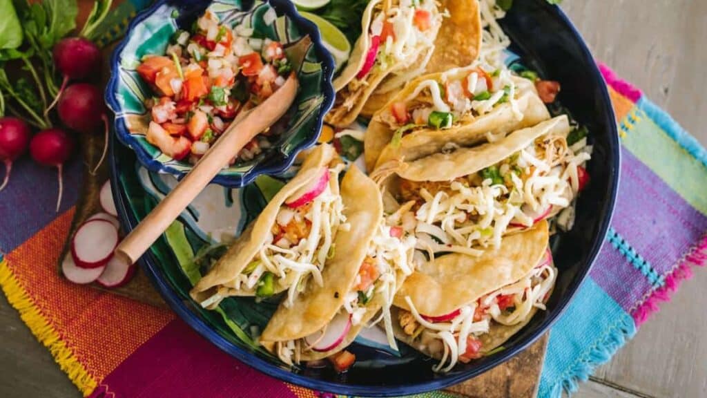 Crispy chicken tacos on a blue plate on a colorful background.