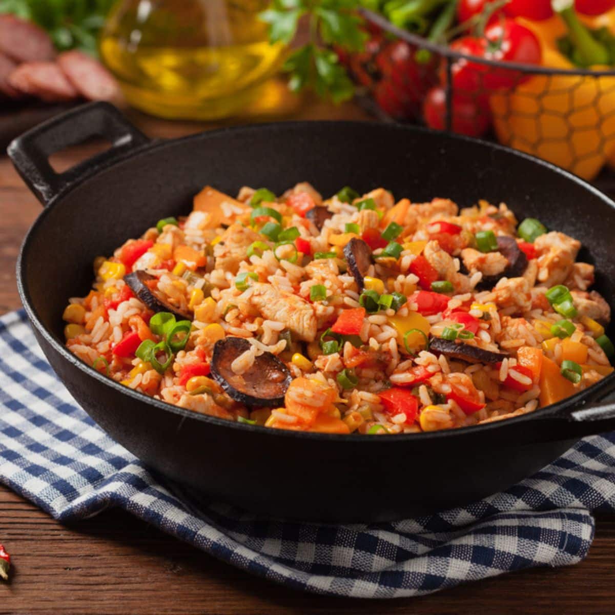 Skillet with sausage, rice, and veggies, with a blue plaid towel underneath skillet.