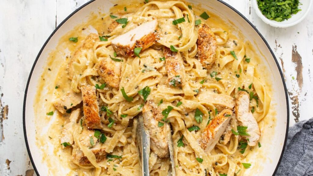 Chicken Alfredo  in a white bowl with tongs in the bowl.