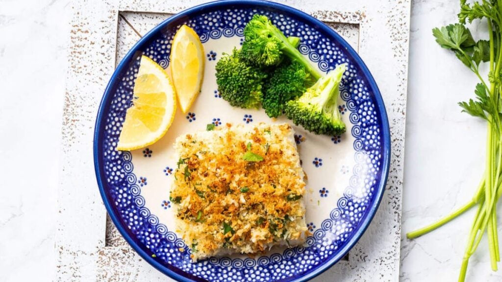 Parmesan crusted cod on a plate with broccoli and lemon slices.