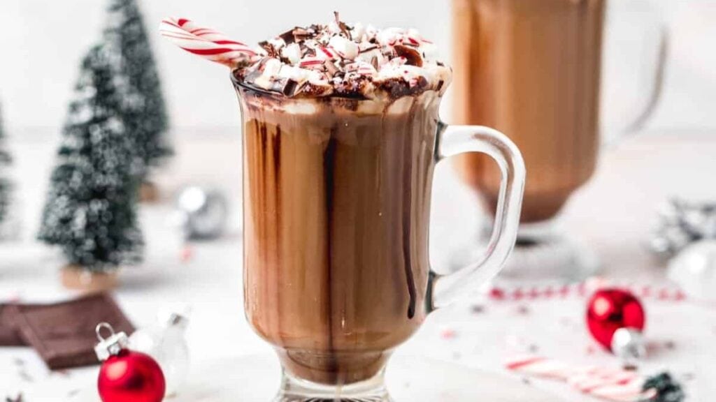 Peppermint mocha in glass mug with Christmas decorations in background.