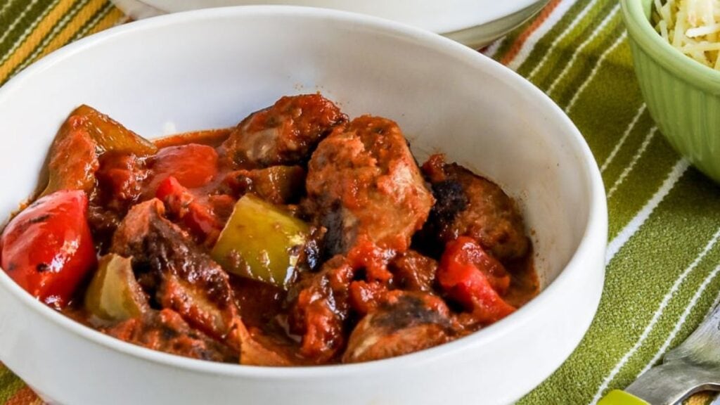 Sausage and peppers in sauce in a white bowl.