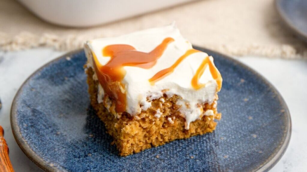 Pumpkin pie poke cake topped with frosting and caramel sauce.
