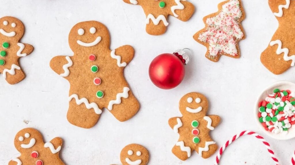 Decorated gingerbread cookies next to a red ornament on a white background.