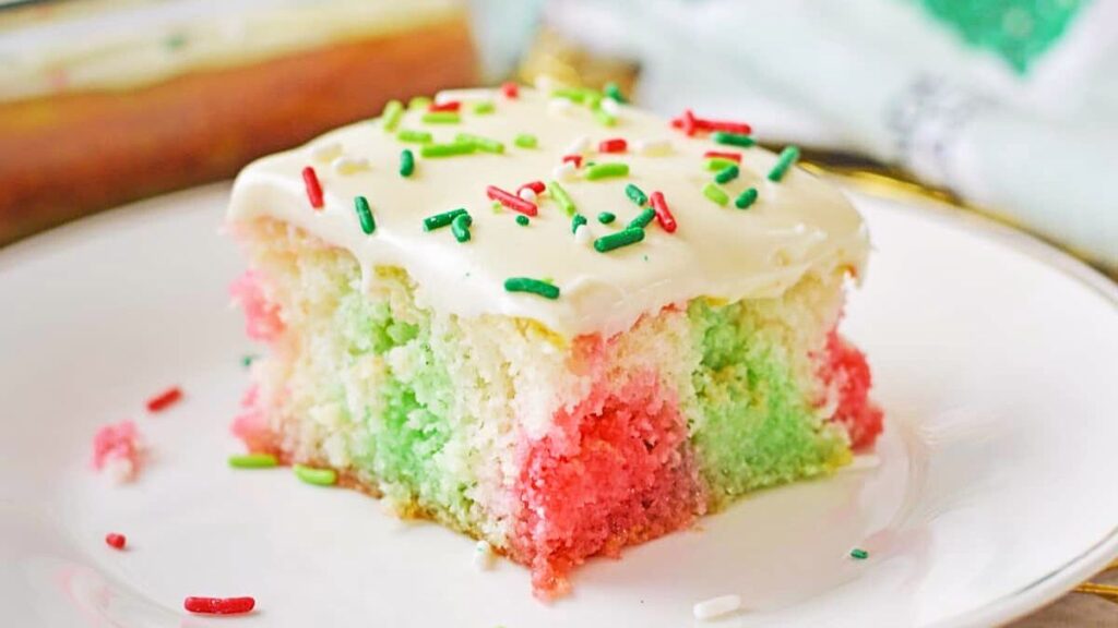 Poke cake that's red and green with frosting and sprinkles.