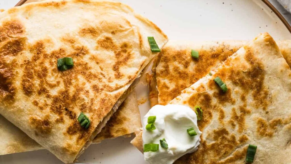 Buffalo chicken quesadillas topped with sour cream on a white plate.