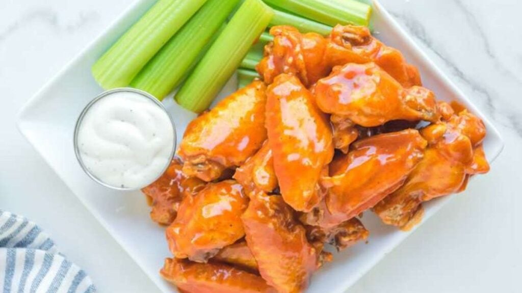 Buffalo wings on a white plate with celery and dipping sauce.