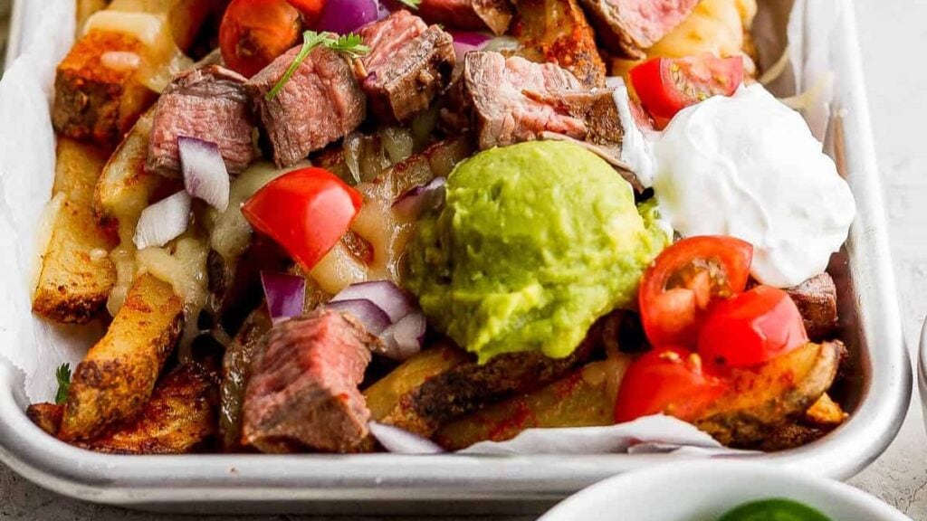 Carne asada fries on a sheet pan topped with guacamole.
