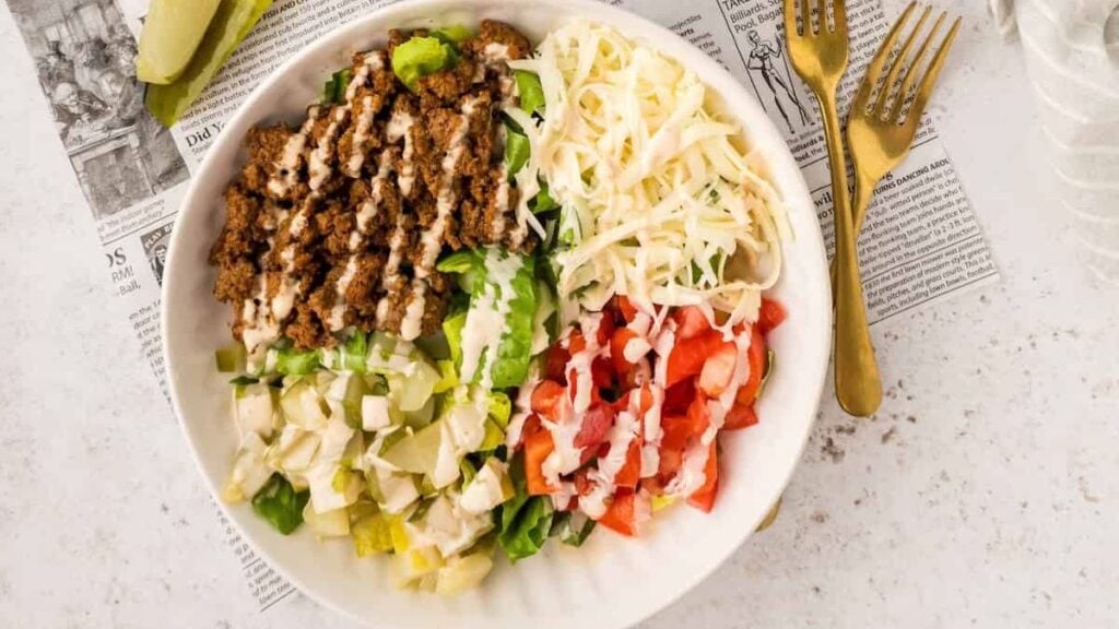 Cheeseburger salad in a white bowl drizzled with sauce.