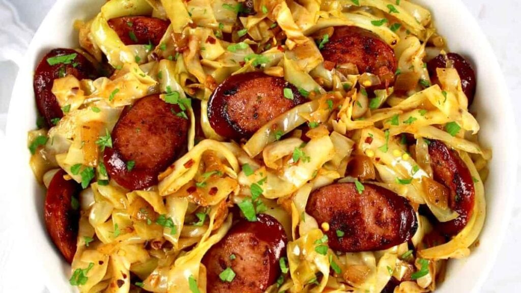 Bowl of fried cabbage and sausage on a table.