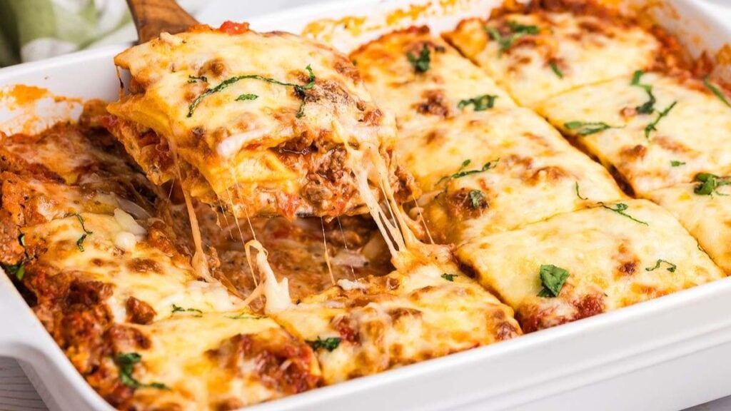 Slice of ravioli lasagna topped with melted, stretchy cheese being lifted from a tray.