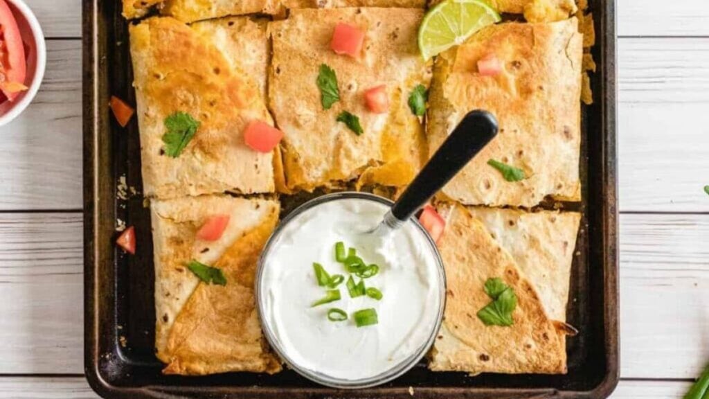 Quesadillas on a sheet pan with sour cream and salsa.