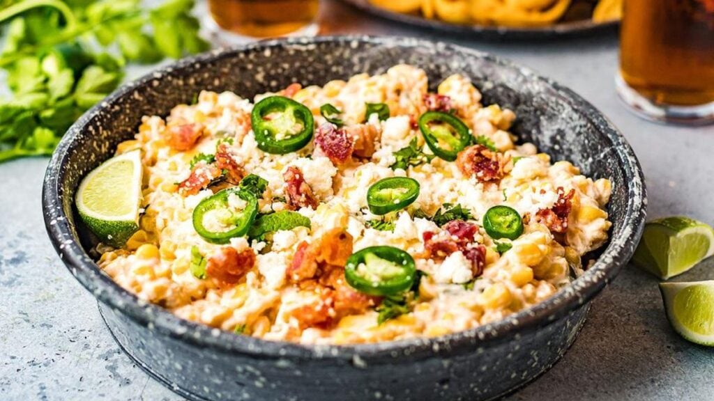 Corn and jalapeno cheese dip with sliced limes and peppers.