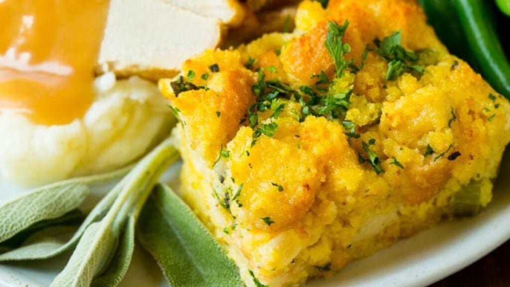 Piece of cornbread dressing on a plate with meat and veggies.