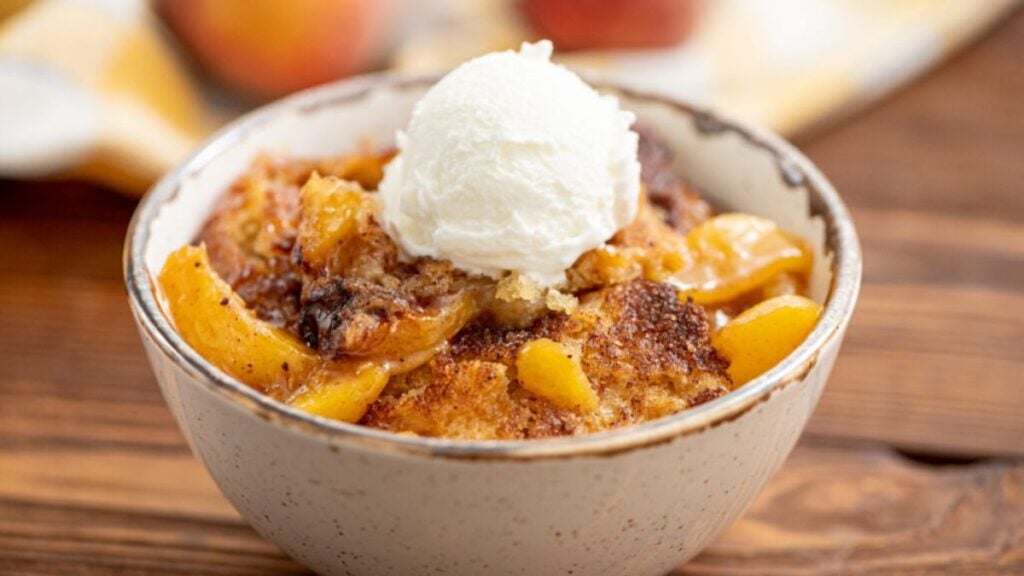 Bowl of peach cobbler topped with ice cream.