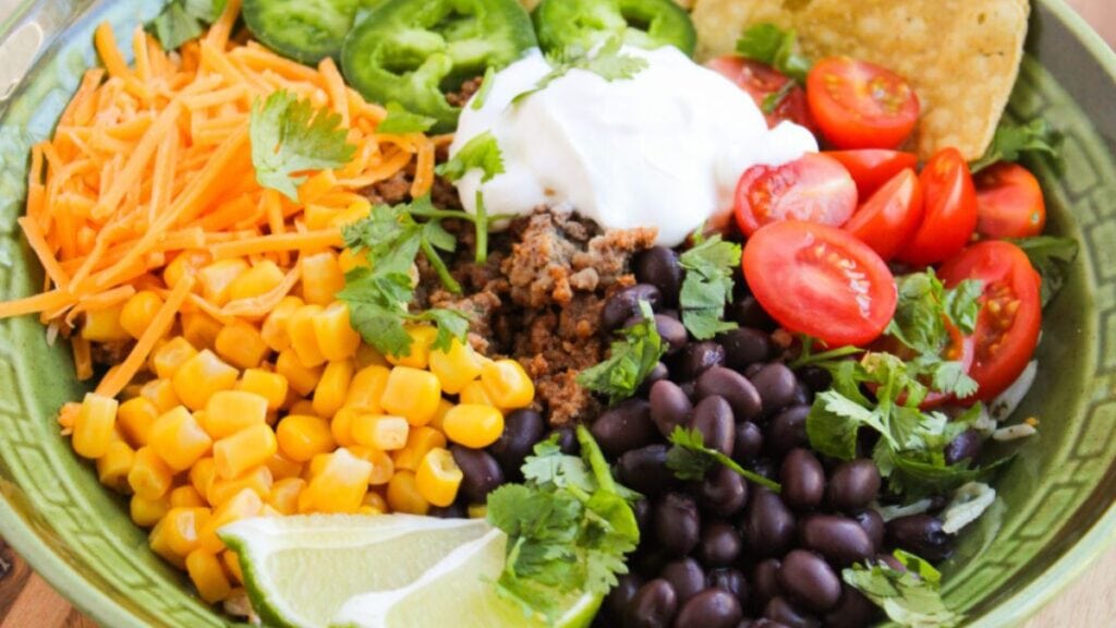 A bowl filled with seasoned taco meat, veggies, and toppings.