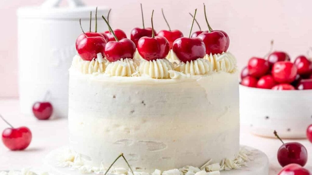 A whole white cake with cherries on top.