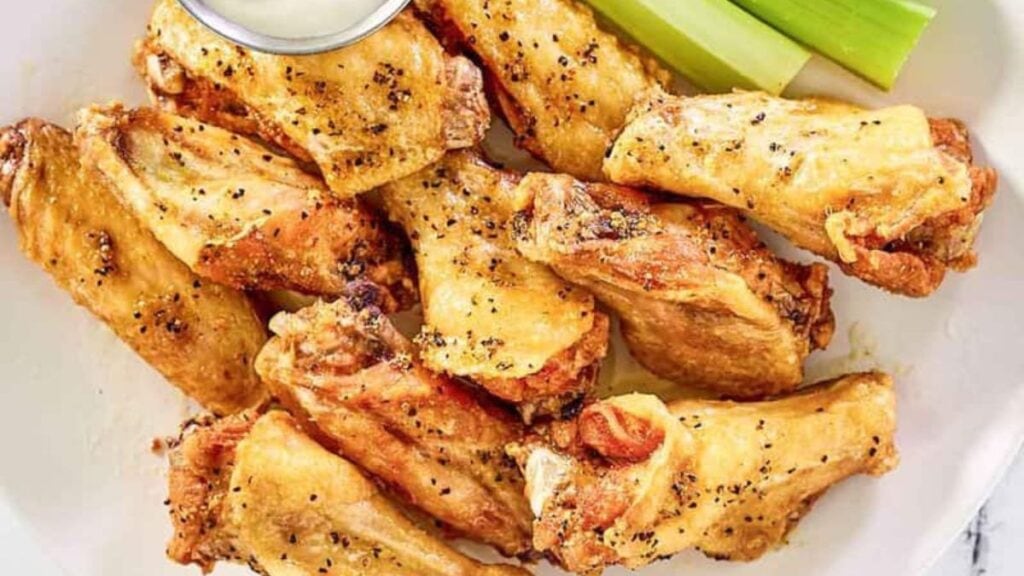 Lemon peppers wings on a white plate with dipping sauce.