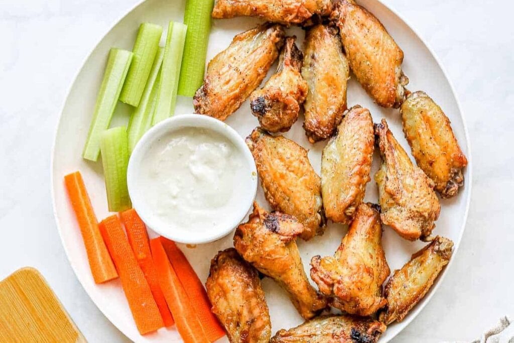 Air fryer chicken wings on plate with vegetables and dipping sauce.