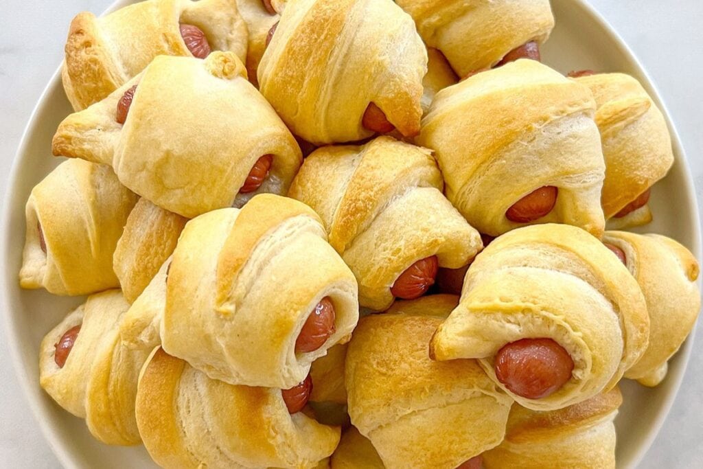Air fryer pigs in a blanket stacked on a plate.