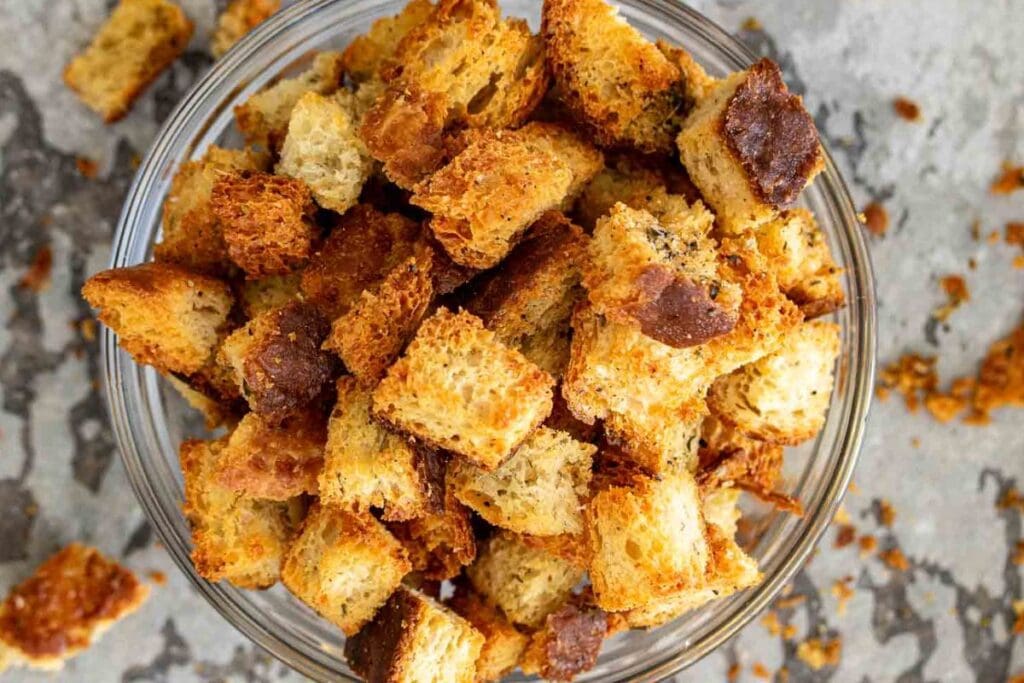 Sourdough croutons in a clear bowl on a marble background.