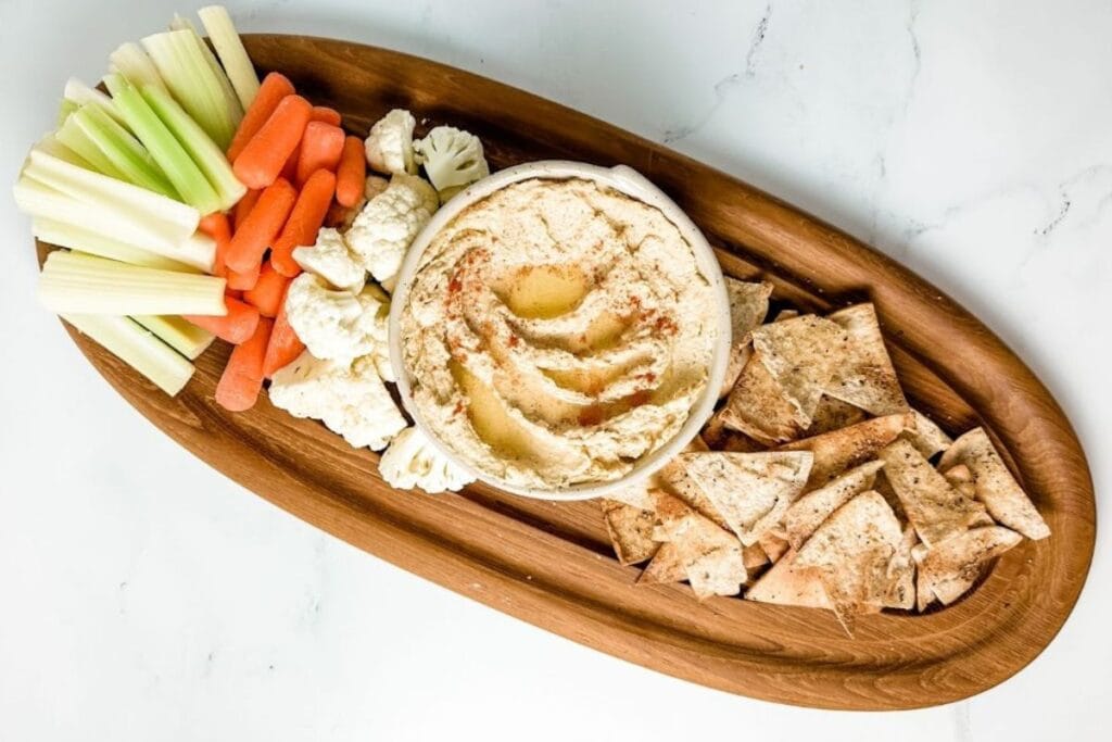 Hummus and pita chips on a wooden plate.