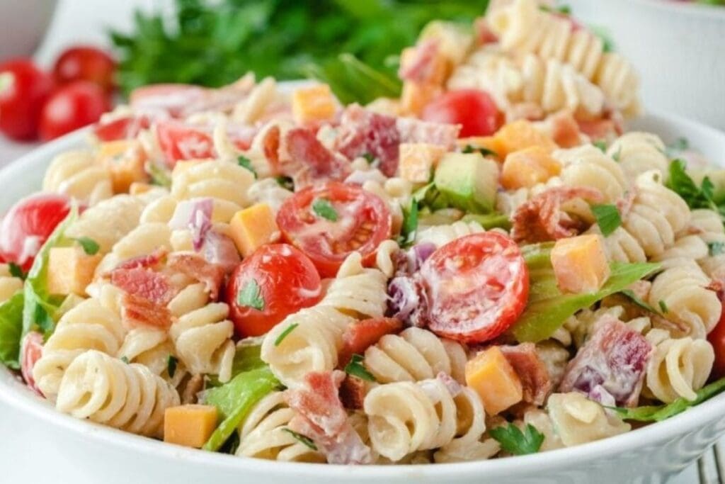 A bowl of pasta salad with rotini pasta, bacon, cherry tomatoes, cheese, and lettuce in a creamy dressing.