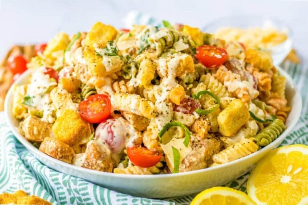 A bowl of pasta salad with rotini pasta, croutons, cherry tomatoes, and a creamy dressing.