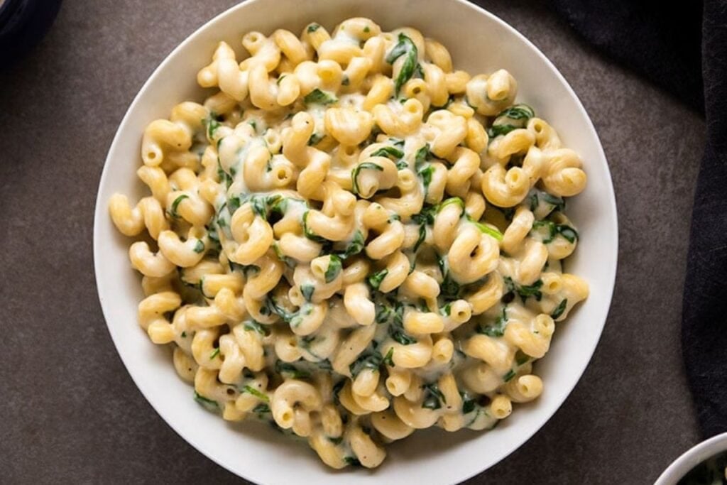 A white bowl of parmesan spinach mac and cheese is shown from above. The pasta is cavatappi, and the sauce is a creamy white sauce with spinach.