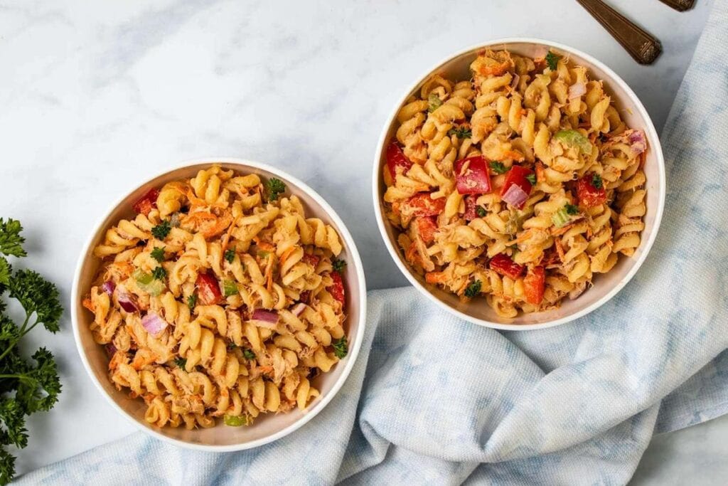Two bowls of pasta salad with tuna, vegetables, and a creamy dressing. A bunch of parsley is in the background.
