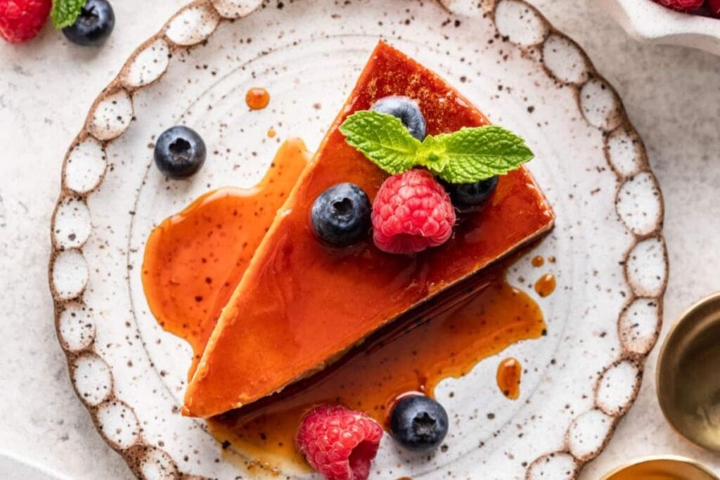 Flan with sauce on brown and white plate topped with berries.