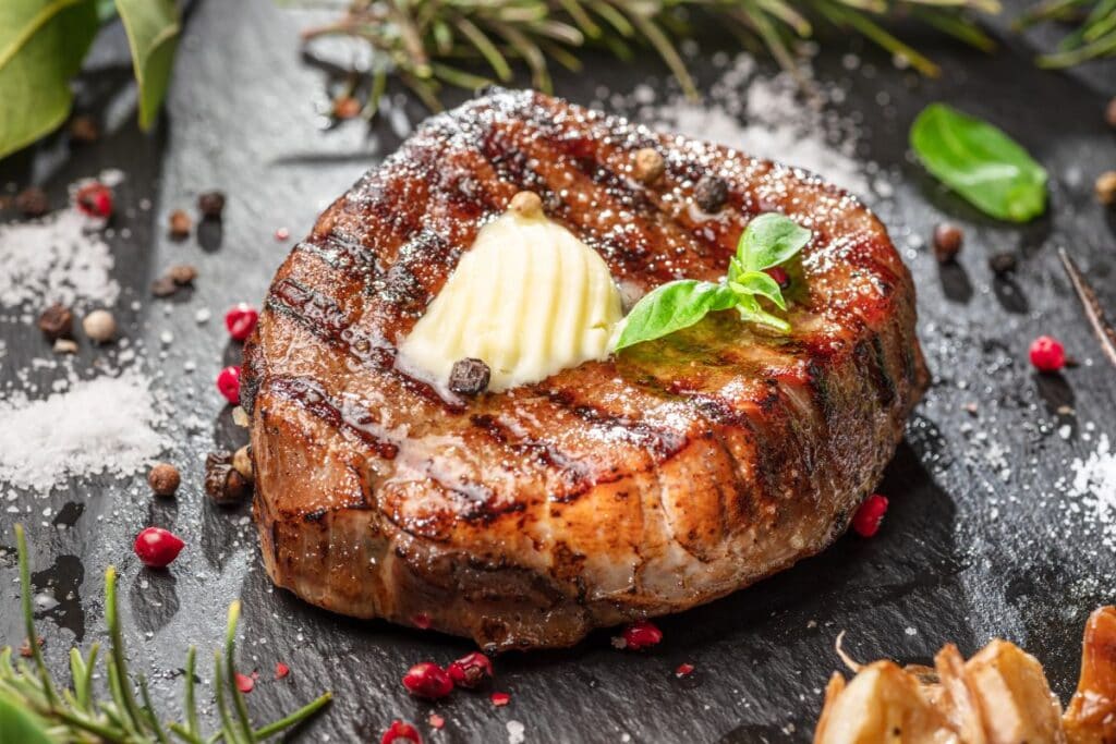 Steak with melting butter on a wooden table with herbs.