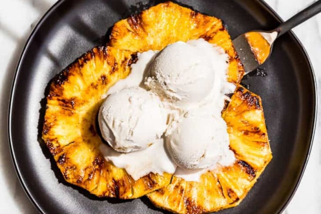 Grilled pineapple with scoops of ice cream.