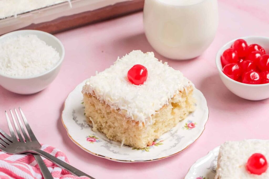 A slice of coconut poke cake with cherry.