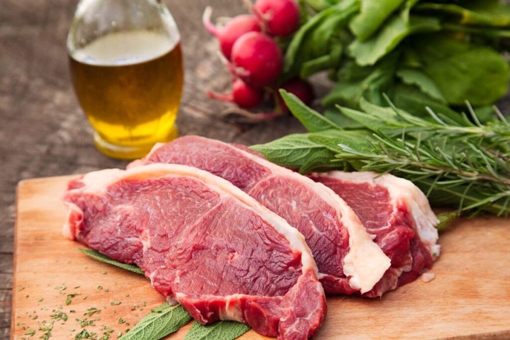 Meat on a cutting board with cooking oil in the background.