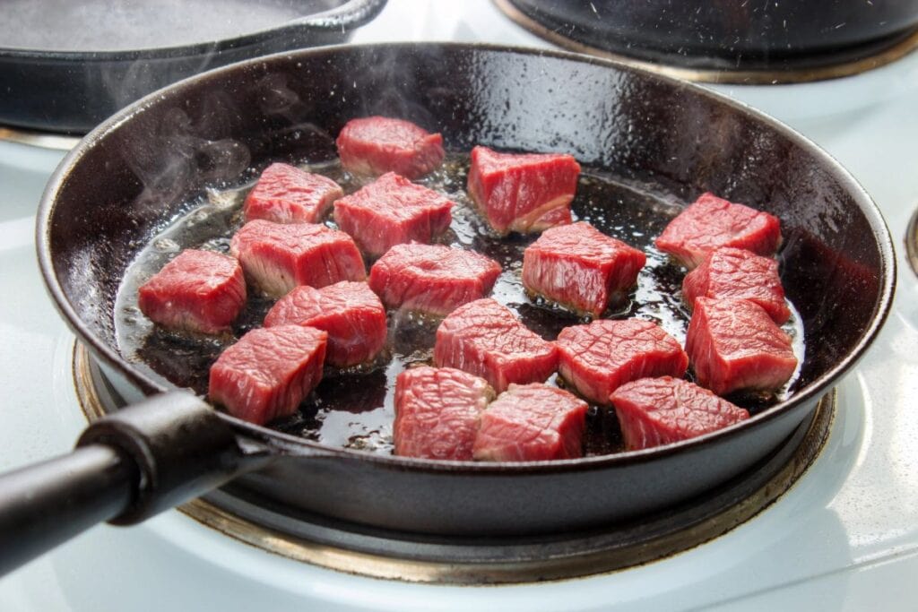 Cubes of meat searing in a black frying pan.